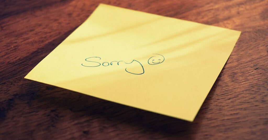 A yellow sticky note with a handwritten apology message and smiley face on a wooden surface.